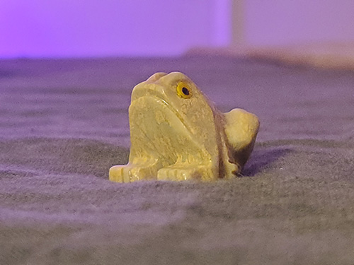 A very small ceramic frog, painted green with yellow eyes.